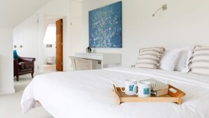 A neatly made bed with a tray of breakfast items, a blue abstract painting on the wall, and a view of a hallway with a door and a chair. - Goodwood Revival 6 Bed Retreat, Secure Parking (Birdham)