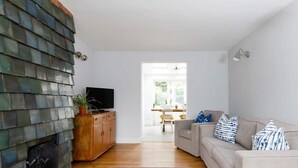 Una sala de estar con chimenea, un sofá, un televisor y un comedor al fondo.