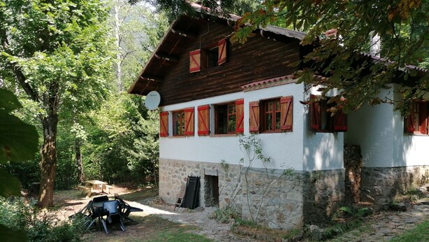 Ein rustikales Holzhaus mit Steinuntergrund, roten Fensterläden und einem Kamin aus Stein.