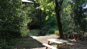 Ein Picknicktisch in bewaldeter Landschaft, ein Feldweg führt zu einem Gebäude.