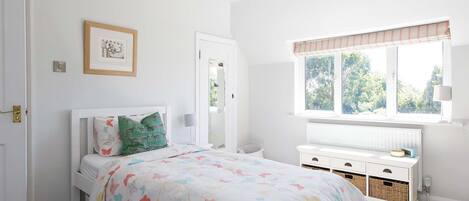 Un dormitorio con cama, ventana con persianas, mesita de noche y radiador.