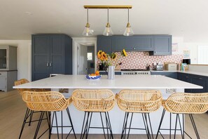 A modern kitchen with a large island, bar stools, and a backsplash with a geometric pattern. - Beach house with pool in West Wittering (West Wittering)