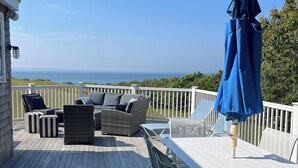 Een houten terras met buitenmeubilair, waaronder een tafel en stoelen, met uitzicht op een prachtig panorama.