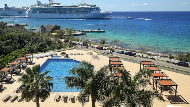 Een resort met een zwembad, ligbedden en uitzicht op de oceaan en cruiseschepen.