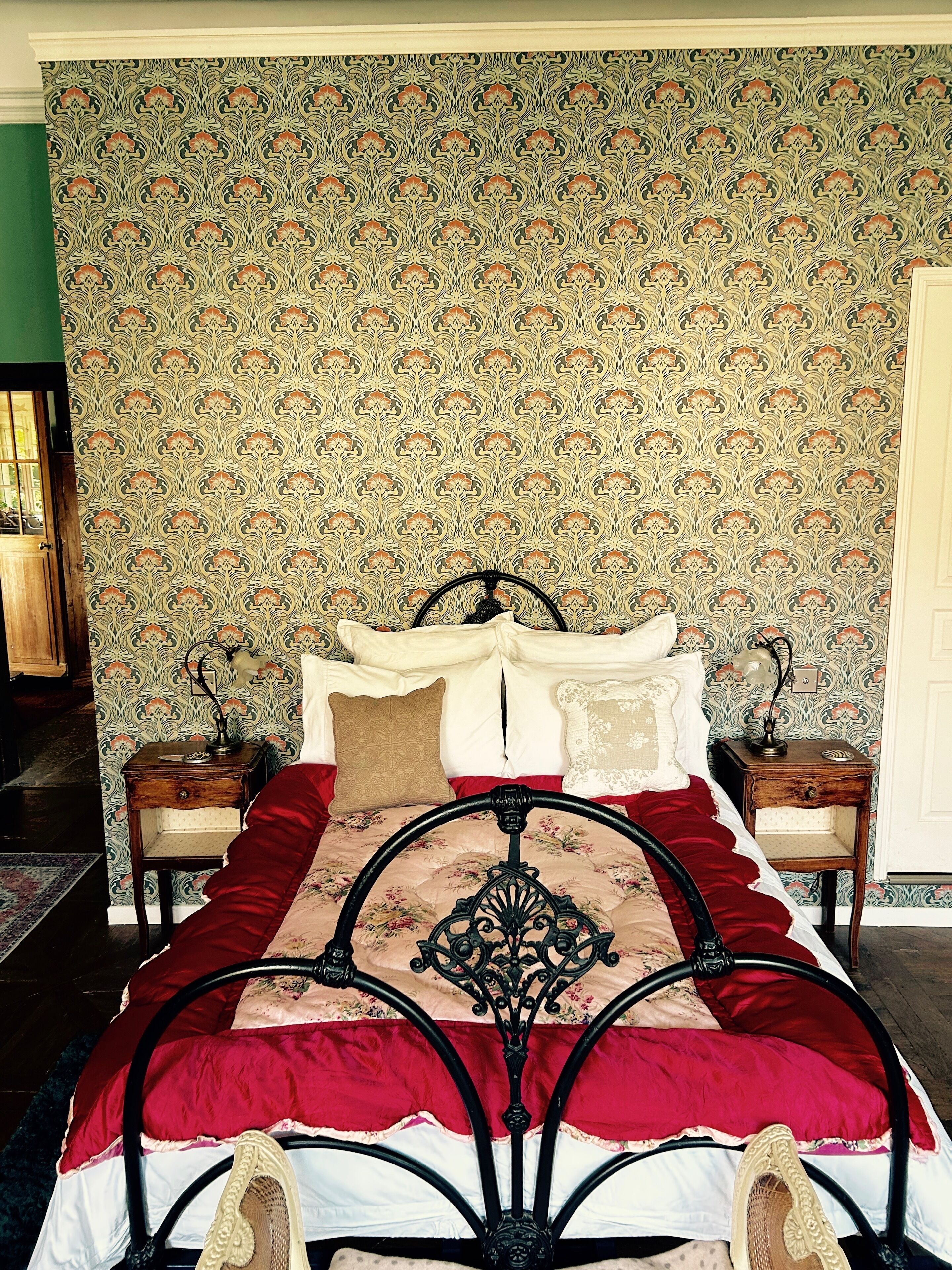 Een slaapkamer met behang met een patroon, een bed met een rood-witte dekbedovertrek en twee nachtkastjes met lampen.