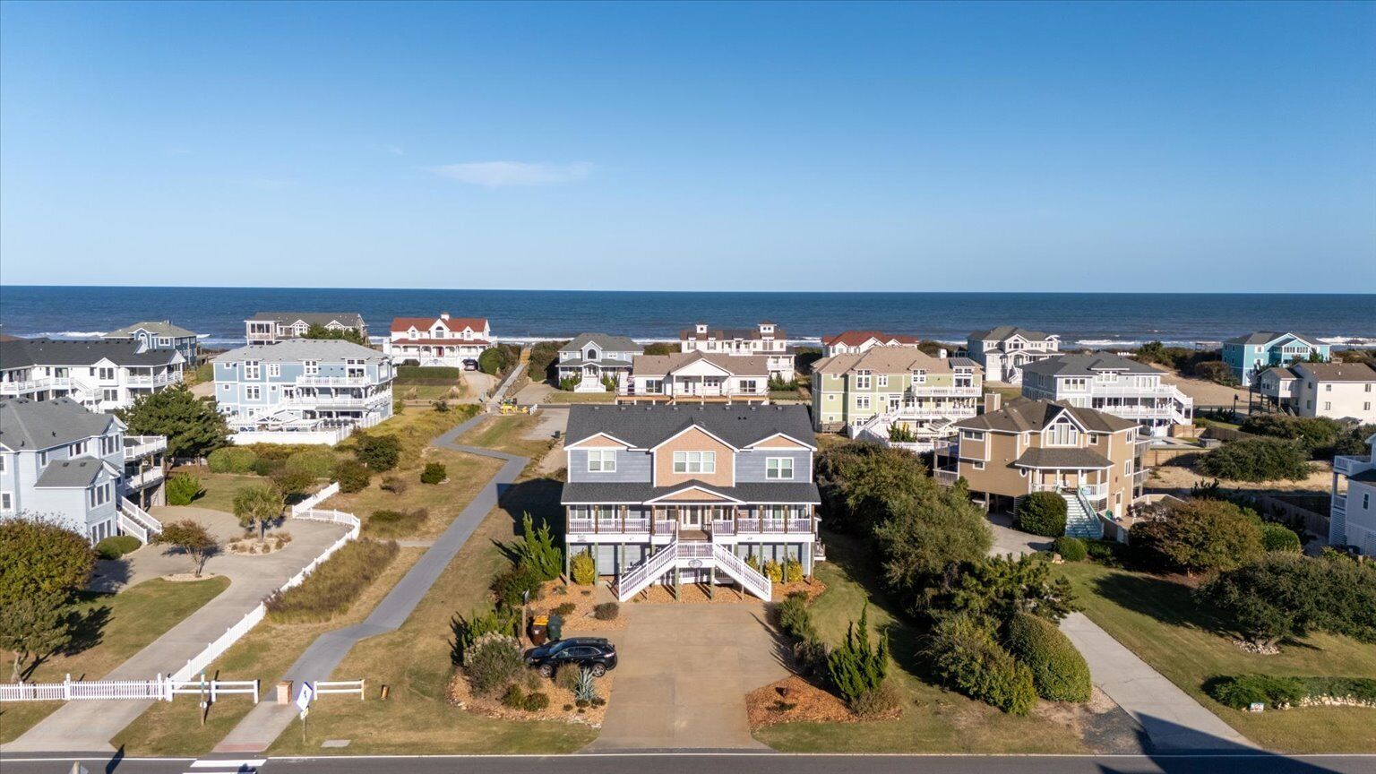 A coastal residential area with houses, a prominent house with a balcony, and a view of the ocean.