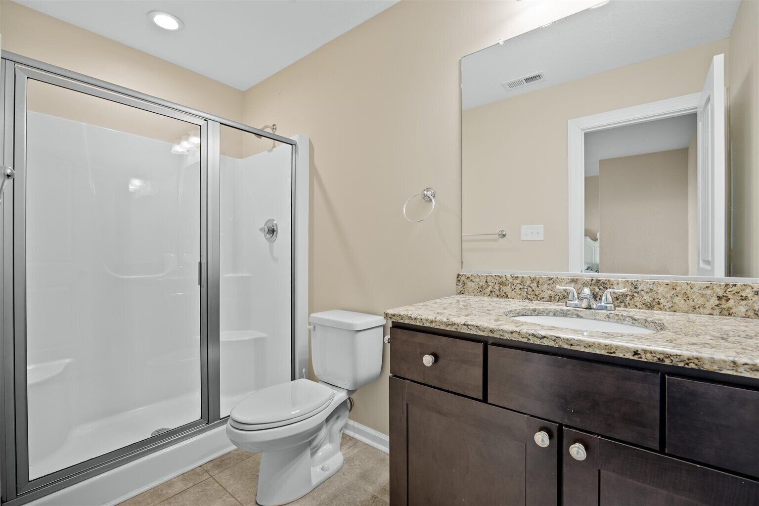 A bathroom with a glass-enclosed shower, a toilet, and a vanity with a granite countertop and a mirror.