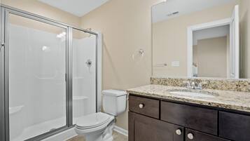 A bathroom with a glass-enclosed shower, a toilet, and a vanity with a granite countertop and a mirror.