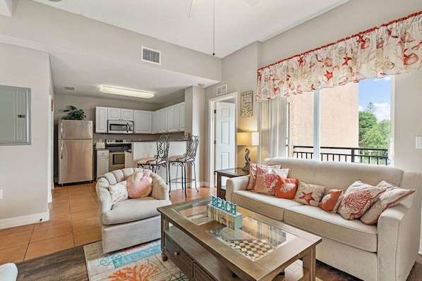 A modern living room with a sofa, coffee table, and a view of the kitchen. - Madeira Bay Resort Bayfront Oasis #202: 2BD/2BA (Madeira Beach)