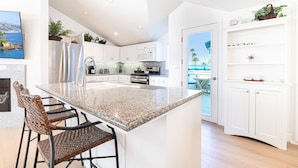Una cocina moderna con armarios blancos, encimeras de granito y una isla grande con taburetes de bar.