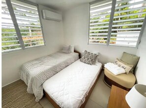 Cozy retreat with two beds, a bedside table, and a window with horizontal blinds.