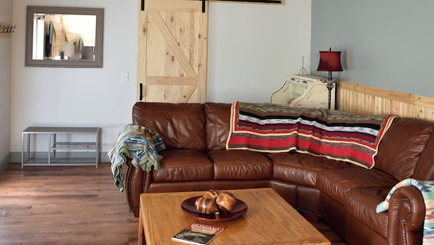 A spacious living room with a brown leather couch, a wooden coffee table, and a ceiling fan. - Mill town location by the river w/hot tub (Bonner-West Riverside)
