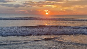A sunset over the ocean with waves approaching the shore.