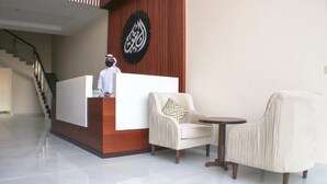 A reception area with a wooden reception desk, a white chair with a patterned cushion, and a round table. - Malath Raqi (Riyadh)