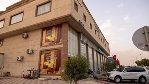 A building with large posters advertising a hotel. There are air conditioning units on the wall, a small tree in front, and a parked car. - Malath Raqi (Riyadh)