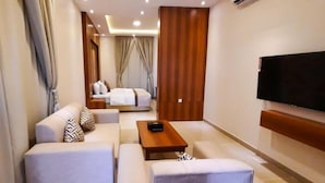 A hotel room with a sofa, a coffee table, a TV mounted on the wall, and a bed with curtains. - Malath Raqi (Riyadh)