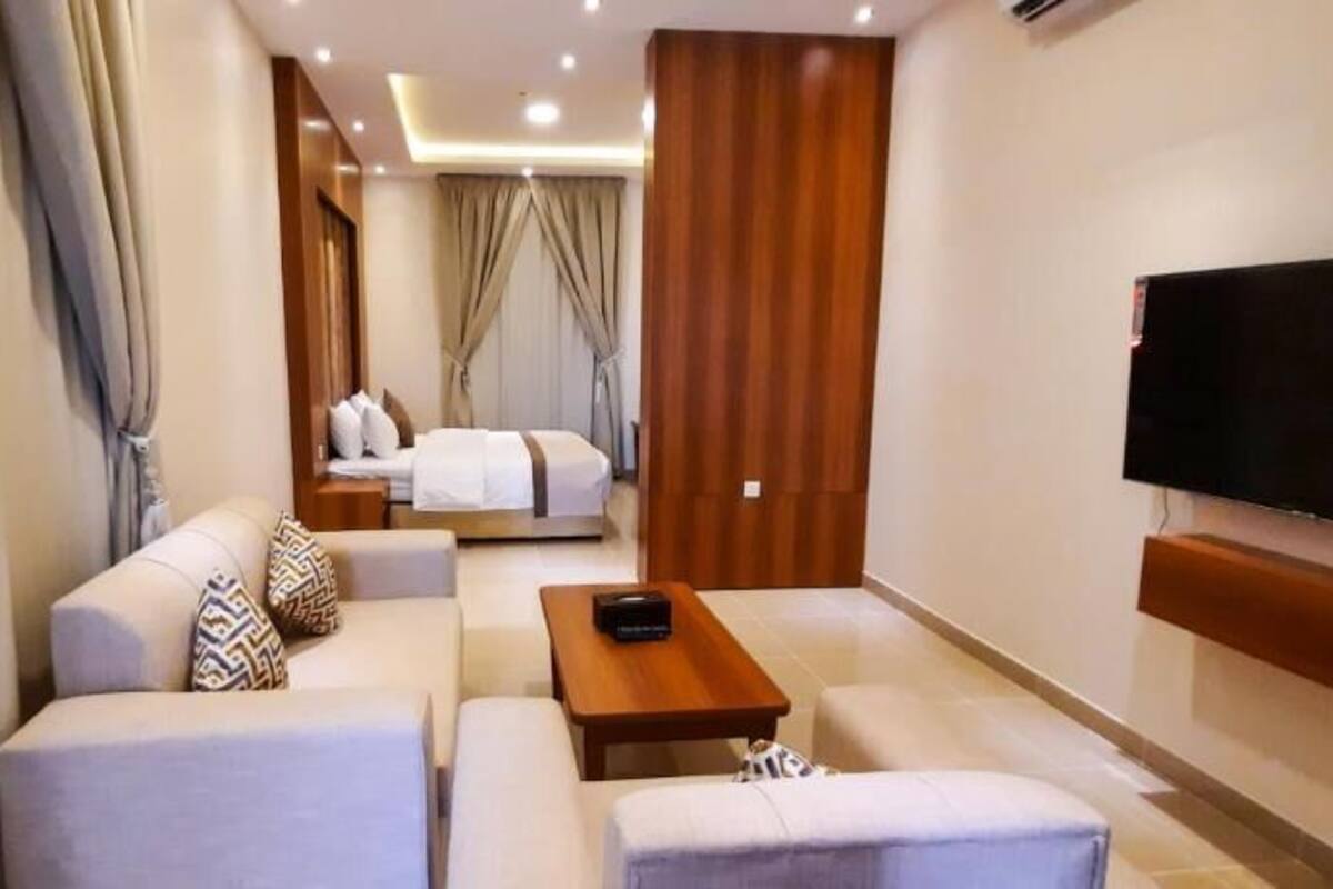 Une chambre d’hôtel équipée d’un canapé, d’une table basse, d’un téléviseur fixé au mur et d’un lit doté de rideaux.