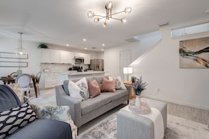 Relax in a stylish living room with a grey sofa, armchair, and dining area, featuring a contemporary chandelier and abstract art.