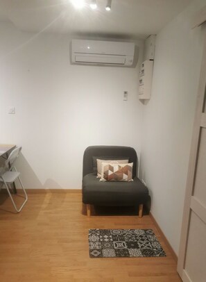 A small, compact room with a single bed, a desk with a chair, and a patterned rug.