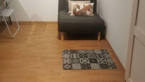 A small, furnished room with a sofa, a patterned rug, a desk with a chair, and an air conditioning unit. - Close to the countryside (Tornac)