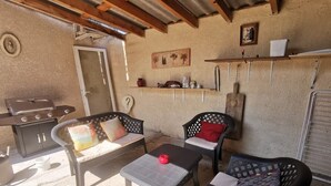 An outdoor patio with a grill, two cushioned chairs, a table, and a shelf with decorative items. - Close to the countryside (Tornac)