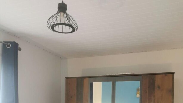A bedroom with a wooden wardrobe, a bed with a blue headboard, and a hanging light fixture. - Close to the countryside (Tornac)