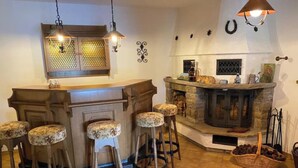 Zona de bar con chimenea de piedra, barra de madera y cuatro taburetes con tapicería floral.