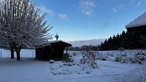 Paisaje nevado con una cabaña de madera y un árbol.