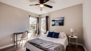 A bedroom with a bed, a desk, a chair, a standing lamp, and a ceiling fan.