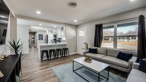 A modern living room with a sofa, coffee table, and a kitchen area in the background.