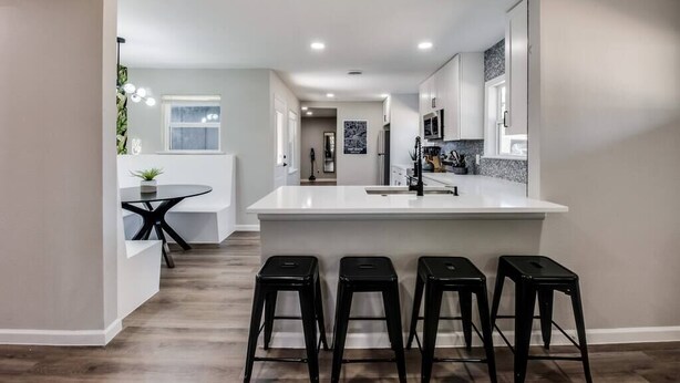 A modern kitchen with a central island, black bar stools, and a small dining area with a table and chairs.