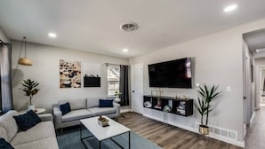 A modern living room with a grey sofa, a white coffee table, and a flat-screen TV mounted on the wall.