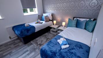 A bedroom with two beds, a patterned wallpaper, and bedside lamps.