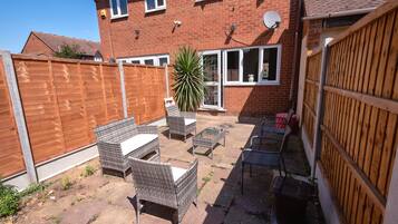 A backyard patio with wicker furniture, a potted plant, and a brick house with a wooden fence.
