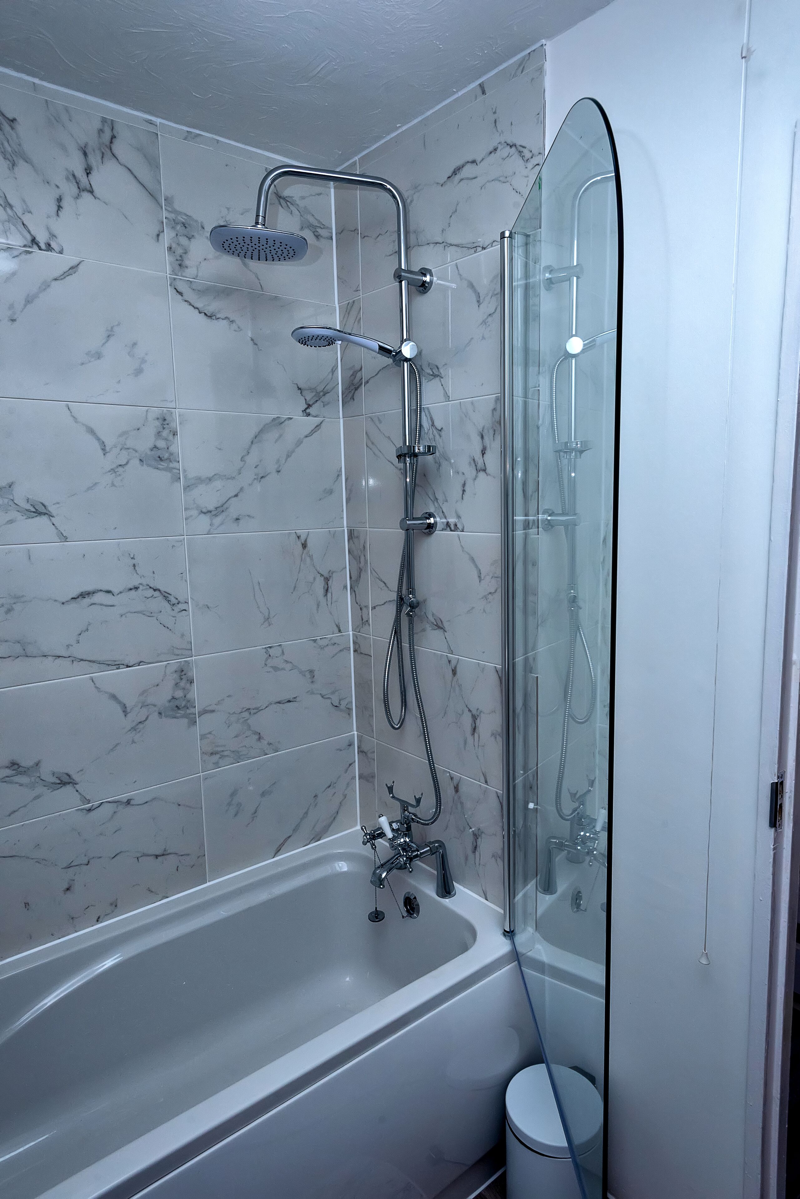 A modern bathroom with a glass-enclosed shower, a standalone bathtub, and marble tiles.