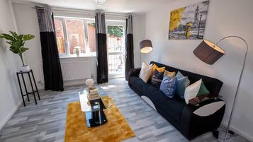 A living room with a black sofa, a coffee table, a floor lamp, and a painting on the wall.