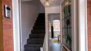 Een trap met beklede treden die leidt naar een overloop, een deurbel aan de muur, en een glas-in-loodraam met bloemmotieven.