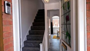 A staircase with carpeted steps leading to a landing, a doorbell on the wall, and a stained glass window with floral designs.