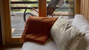 A room with a bed, a chair, and a view of a landscape through a glass door.