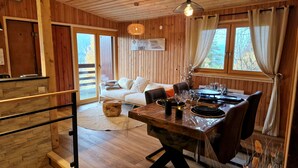 A wooden interior with a dining table set for four, a sofa, and a wooden staircase.