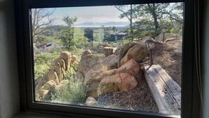 Una ventana con vista a un terreno rocoso al aire libre, que incluye un farol y árboles.