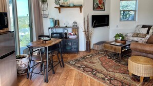 Una sala de estar moderna con una mesa de comedor de madera, sillas negras, un sofá, un televisor y un ventanal con cortinas.