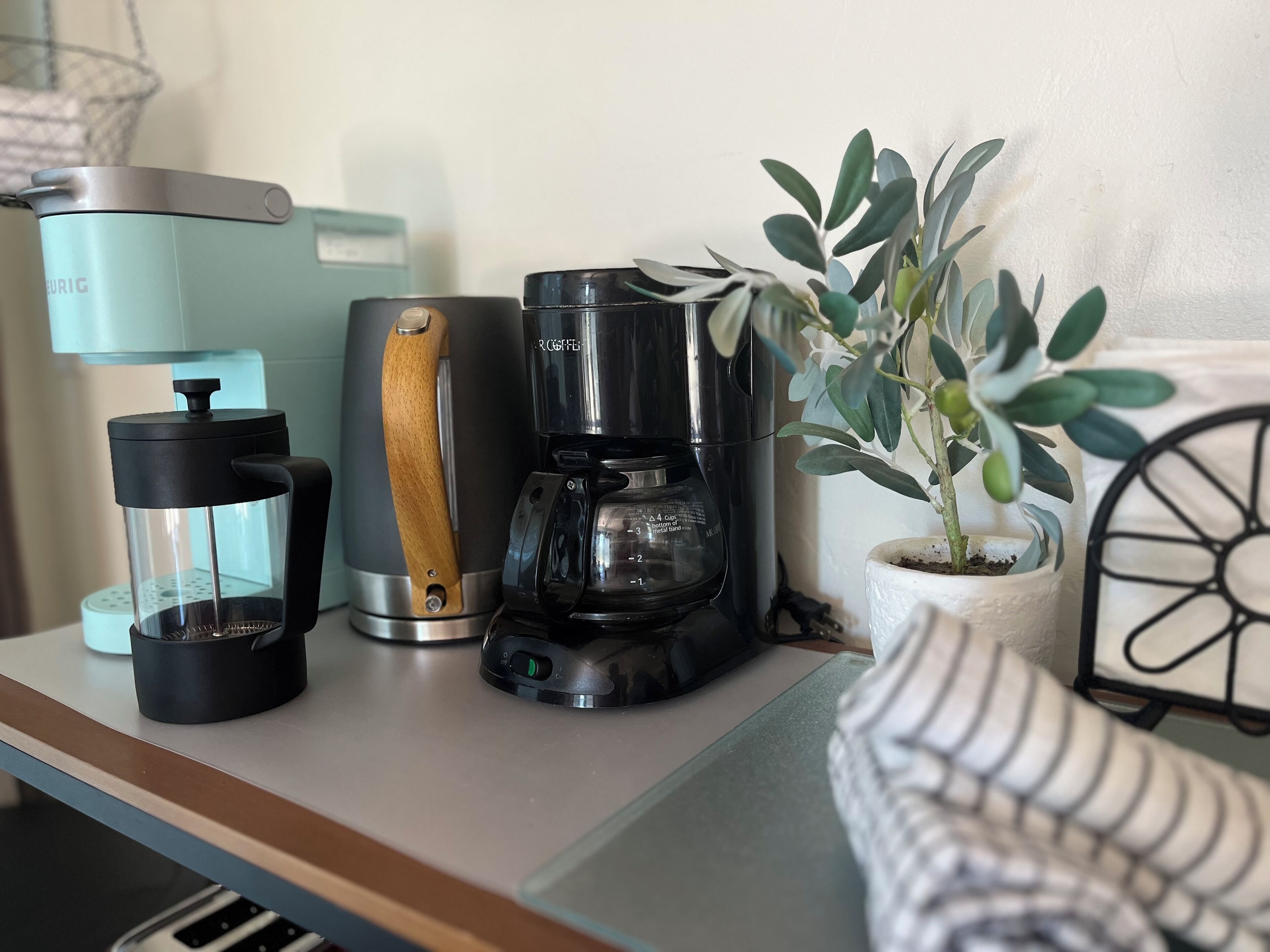Een aanrecht met een koffiezetapparaat, een waterkoker en een potplant.