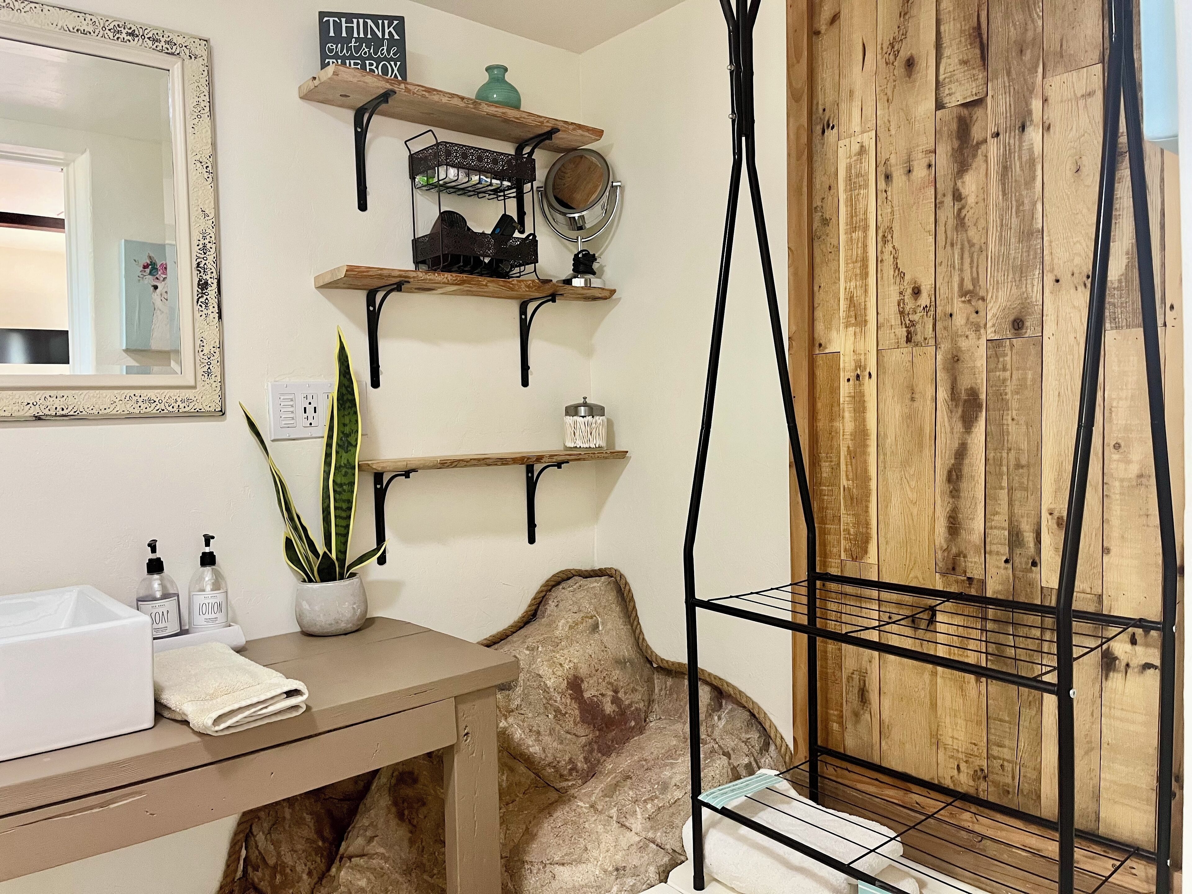 A bathroom with a wooden vanity, a mirror, and shelves with toiletries.