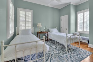 A bedroom with two beds, a bedside table with a lamp, a door, and a window with blinds.