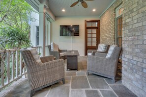 A covered patio with wicker furniture, a ceiling fan, and a stone floor.