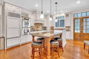 A spacious kitchen with white cabinetry, a central island with stools, and a large wooden door. - Heart of Historic Pinehurst, Golf, Saltwater Pool (Pinehurst)