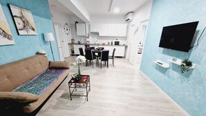 A modern living room with a sofa, a coffee table with flowers, a dining area with chairs, and a kitchen in the background. - 301, 2 bedrooms,close Playa las Americas&free wifi (Playa de la Américas)