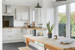 A modern kitchen with white cabinets, a wooden countertop, a gas stove, and a large window with a view of greenery.