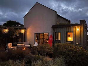 A modern house with a large glass door, a small attached wooden structure, and a red surfboard outside.
